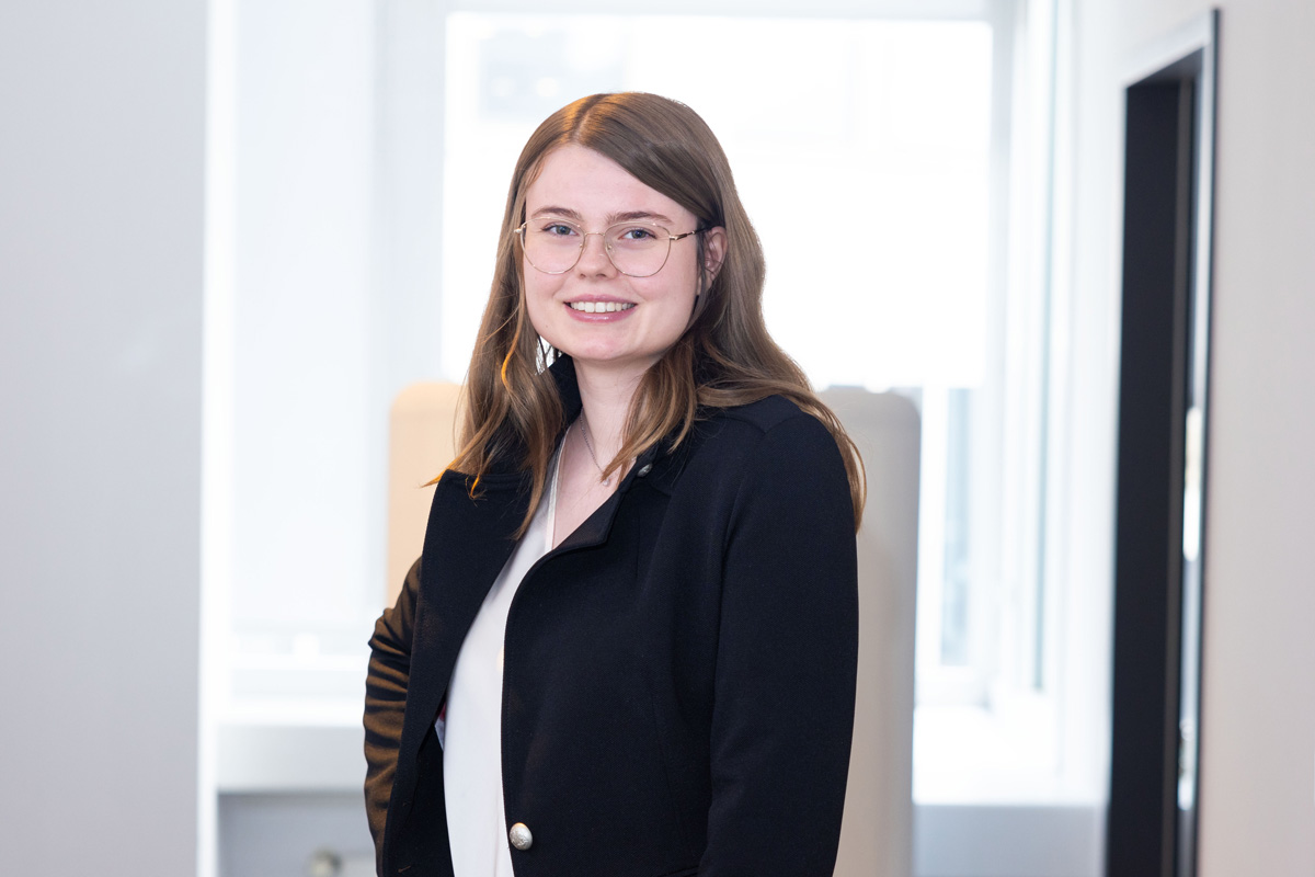 Porträtfoto einer Frau mit langen Haaren im Business-Outfit.
