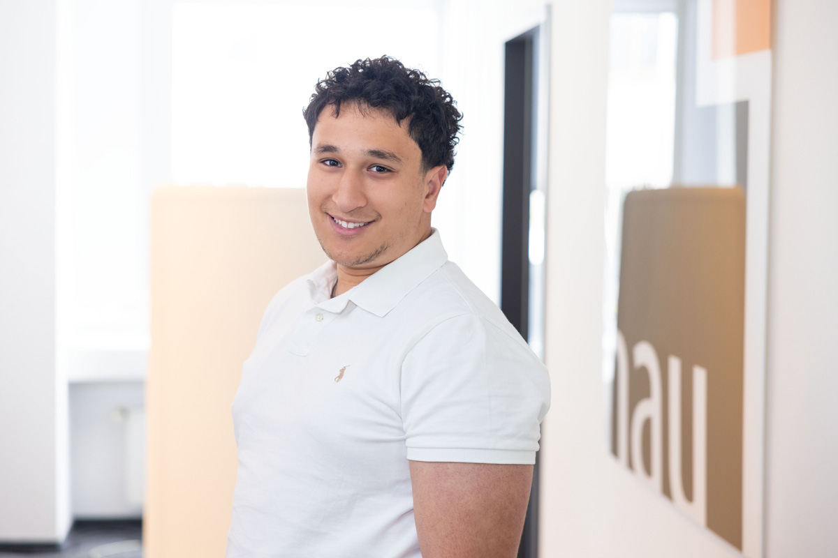 Porträtfoto eines Mannes in weißem Hemd vor Bürotür.
