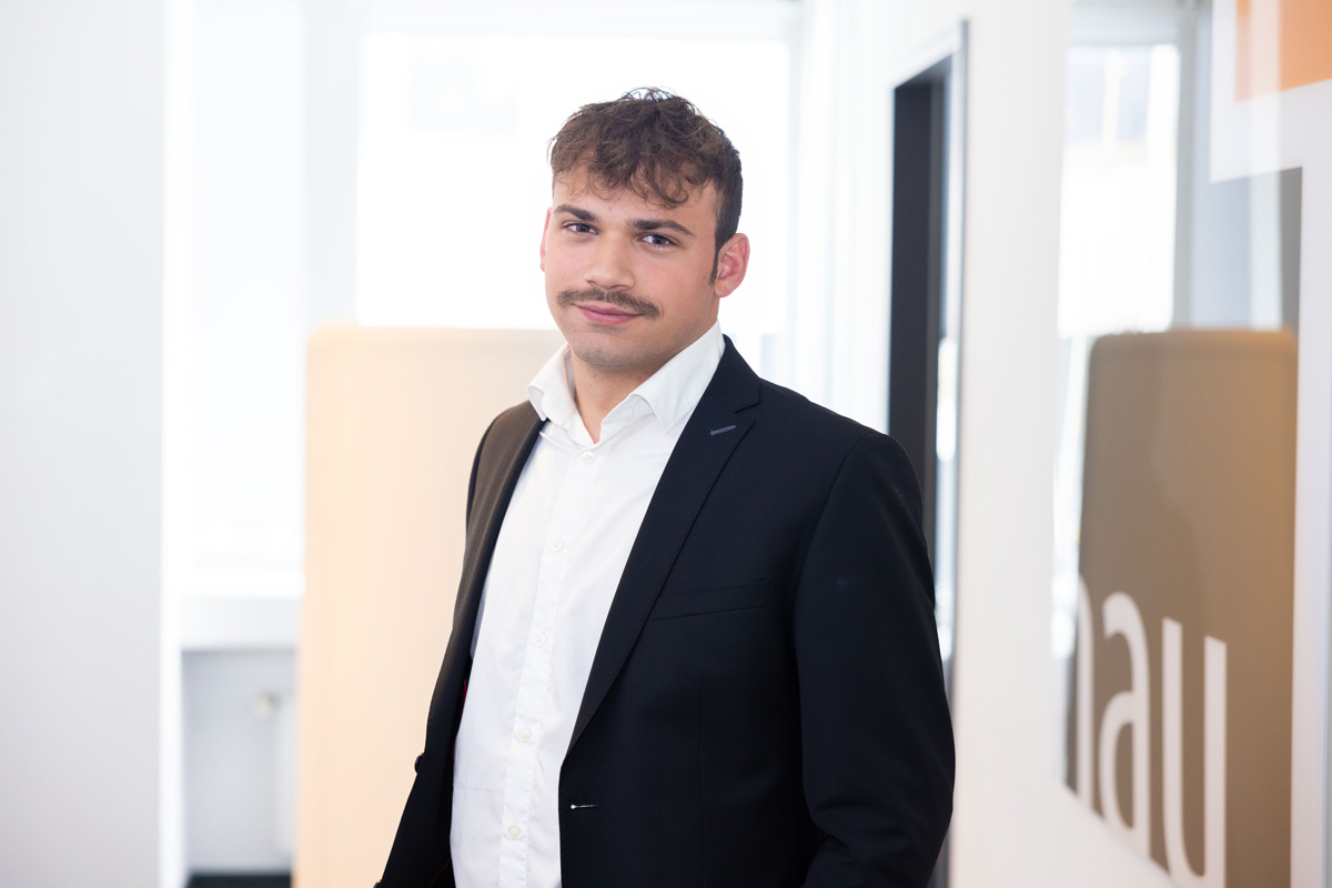 Porträtfoto eines Mannes vor einem Büro-Hintergrund.