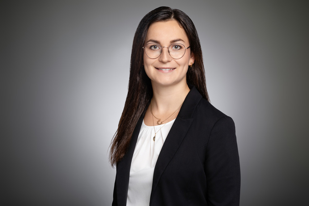 Porträtfoto einer Frau im Business-Outfit vor neutralem Hintergrund.