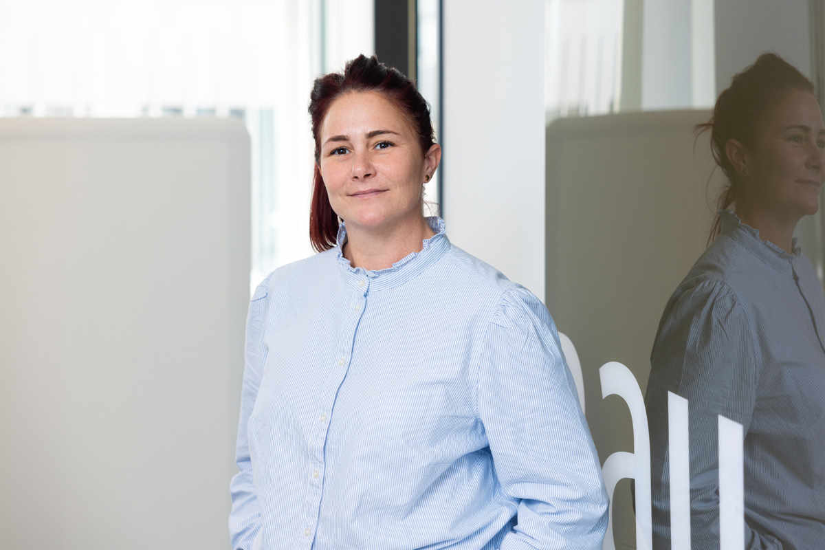 Porträtfoto einer Frau im blauen Hemd in einem Büroflur.